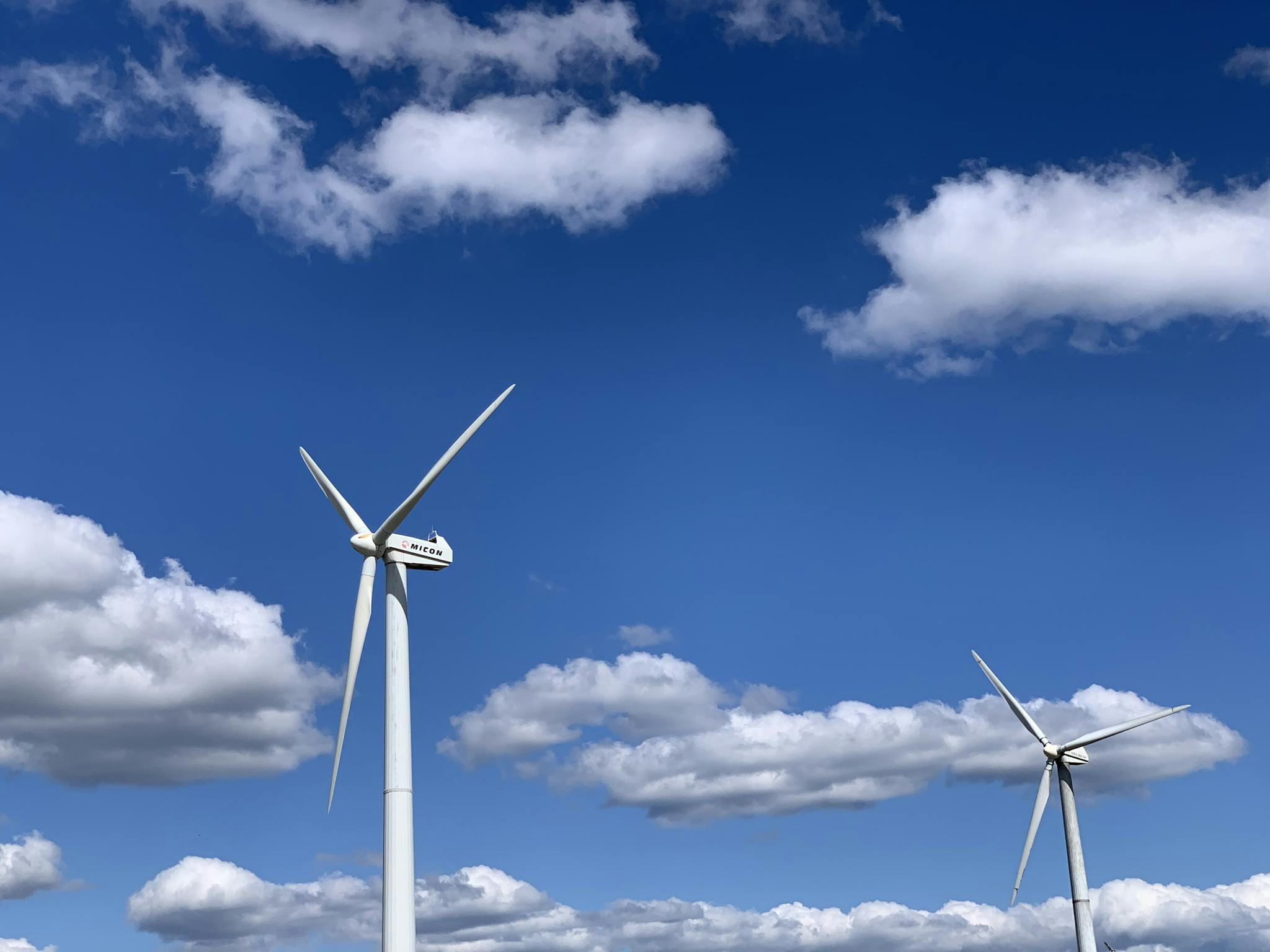 Low angle of white modern windmill turbines generating energy against cloudy blue sky on sunny day
