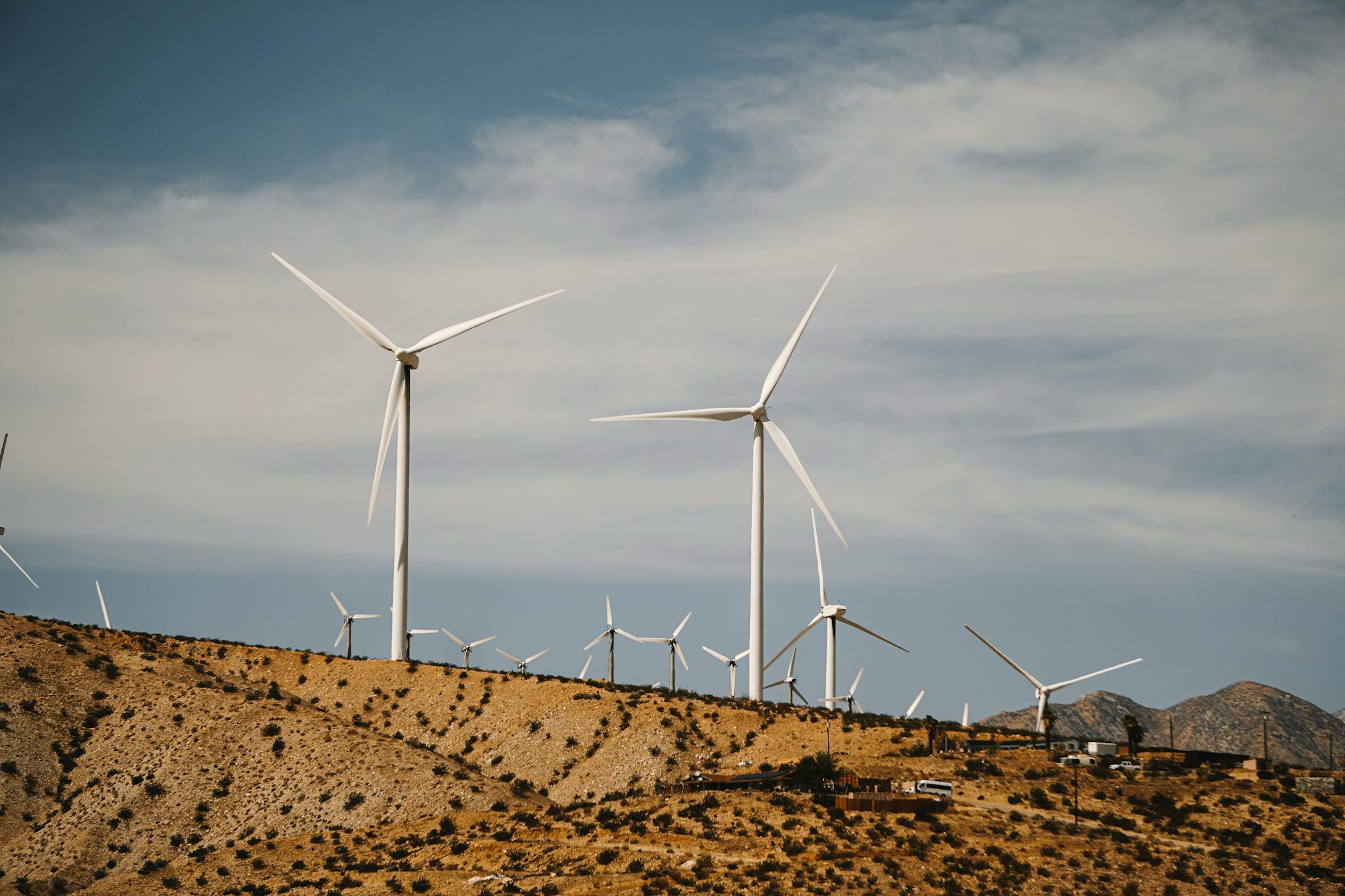 Wind turbines on a sunny desert hillside with clear skies, showcasing renewable energy use.